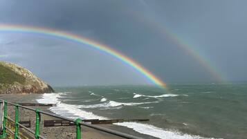 A coastal scene with a rainbow, waves, and a railing.