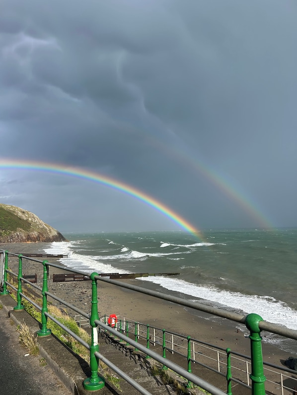 A coastal scene with a rainbow, waves, and a railing. - Awel Mor (Criccieth)
