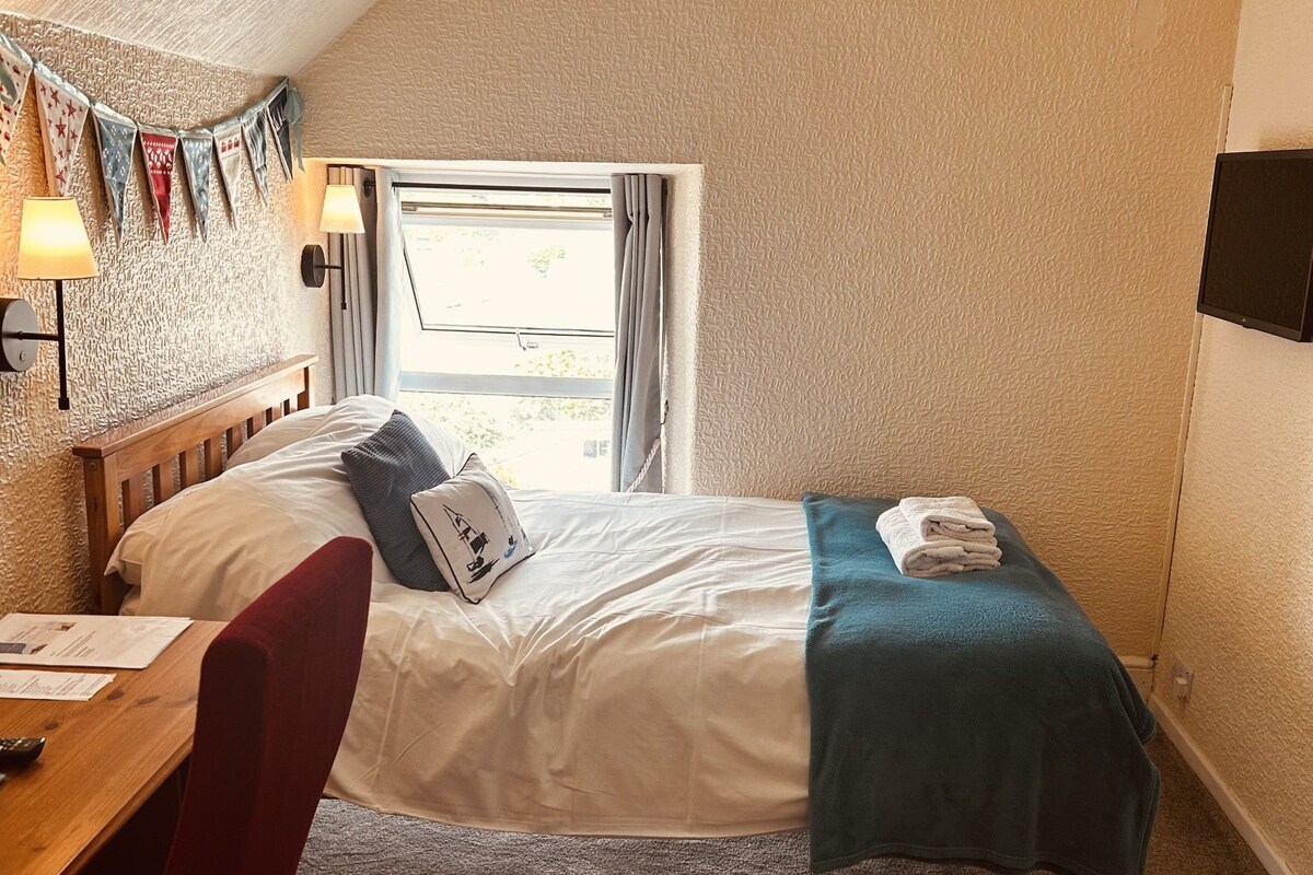 A bedroom with a bed, bedside lamps, a window, and a wall-mounted TV.