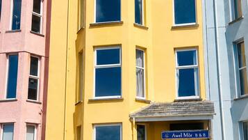 A multi-story building with a yellow facade, a ground-floor entrance labeled 'Awel Môr B&B,' and a sign indicating vacancies.