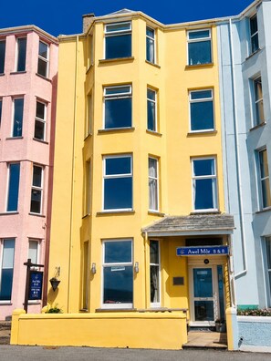 A multi-story building with a yellow facade, a ground-floor entrance labeled 'Awel Môr B&B,' and a sign indicating vacancies. - Awel Mor (Criccieth)