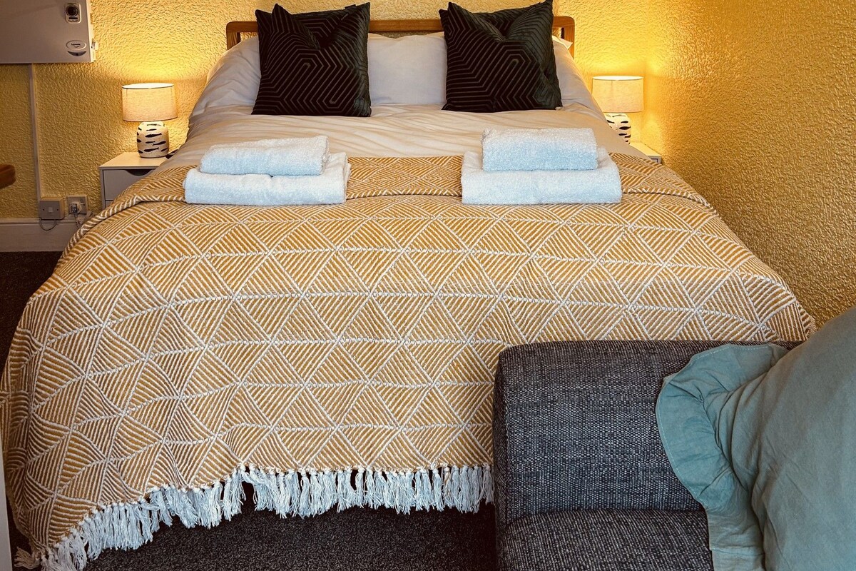 A hotel room with a bed, two bedside lamps, a painting on the wall, and a small table with a lamp.