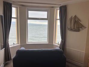 Habitació amb finestra panoràmica que dona al mar, un sofà de color fosc i un objecte decoratiu fixat a la paret.