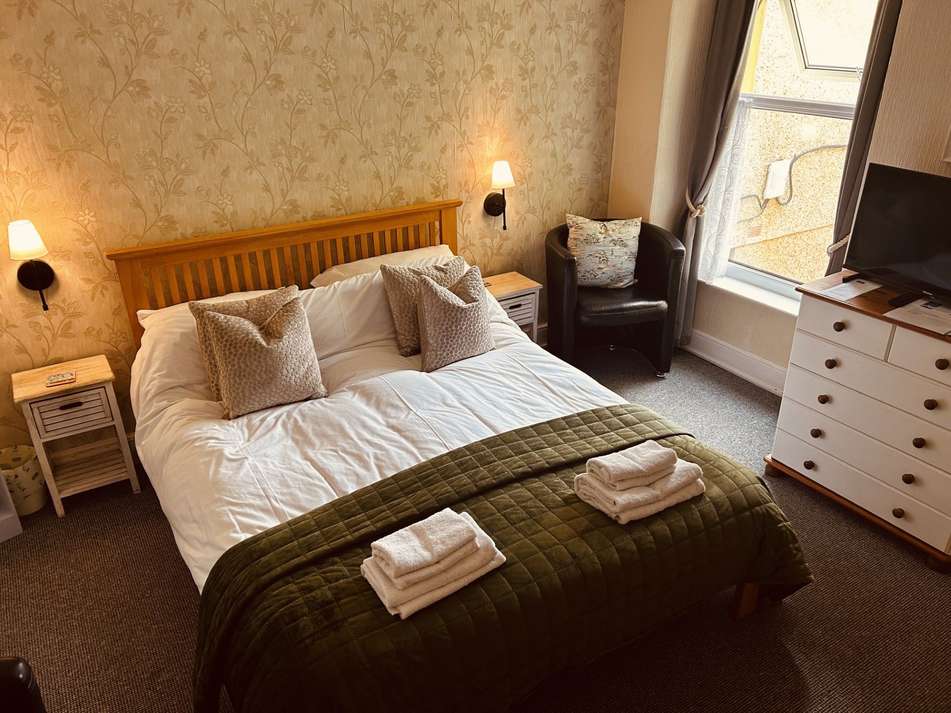A hotel room with a bed, two bedside lamps, a chair, a dresser, and a television.