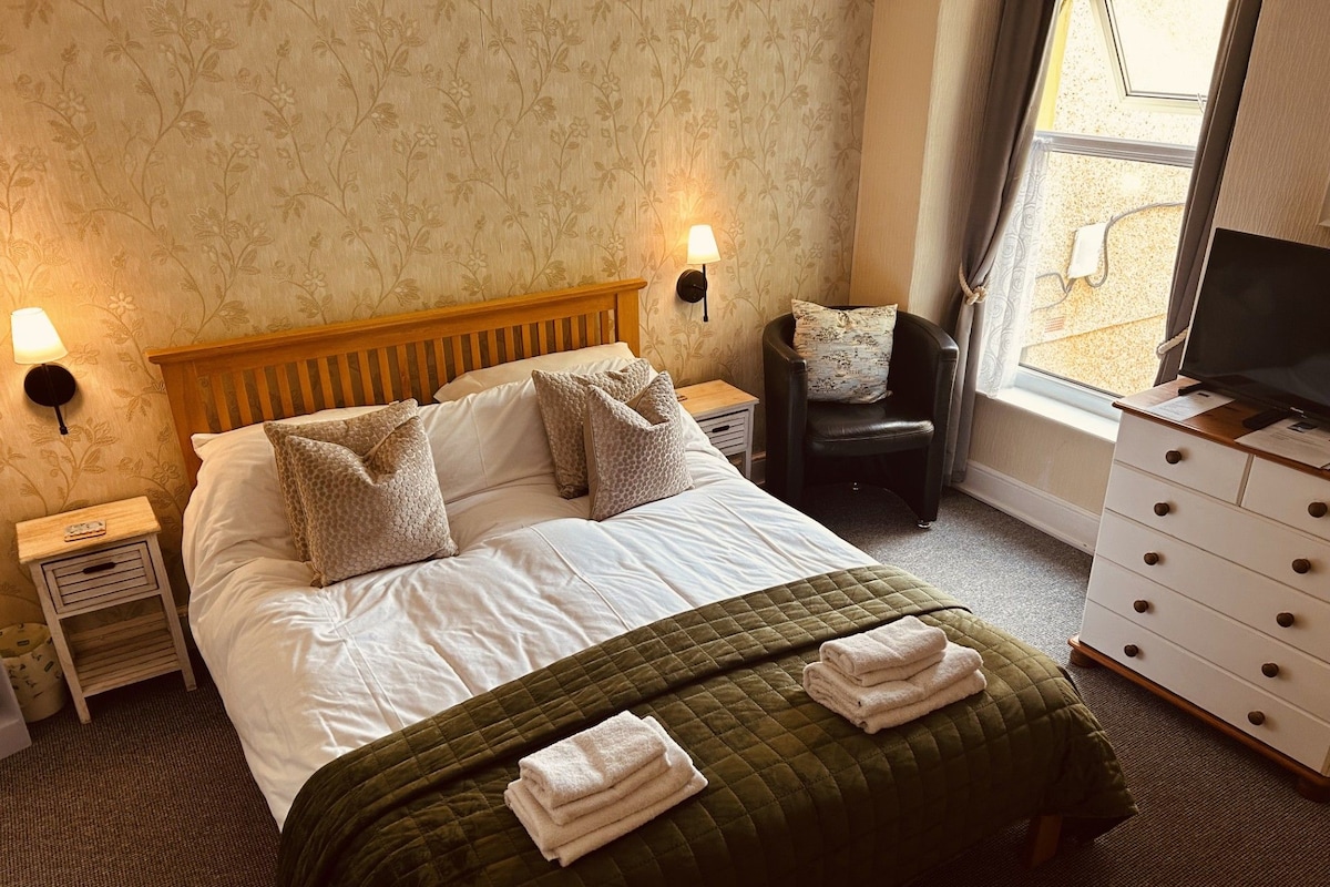 A hotel room with a bed, two bedside lamps, a chair, a dresser, and a television.