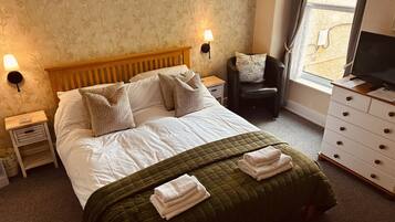 A hotel room with a bed, two bedside lamps, a chair, a dresser, and a television.