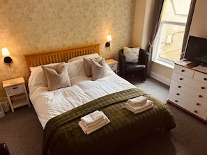 A hotel room with a bed, two bedside lamps, a chair, a dresser, and a television. - Awel Mor (Criccieth)