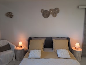 A bedroom with a bed, two bedside lamps, a wall-mounted decorative piece, and a nightstand. - Guest room 'Chambre Retour De Plage' with shared pool, shared terrace and Wi-Fi (La Devise)