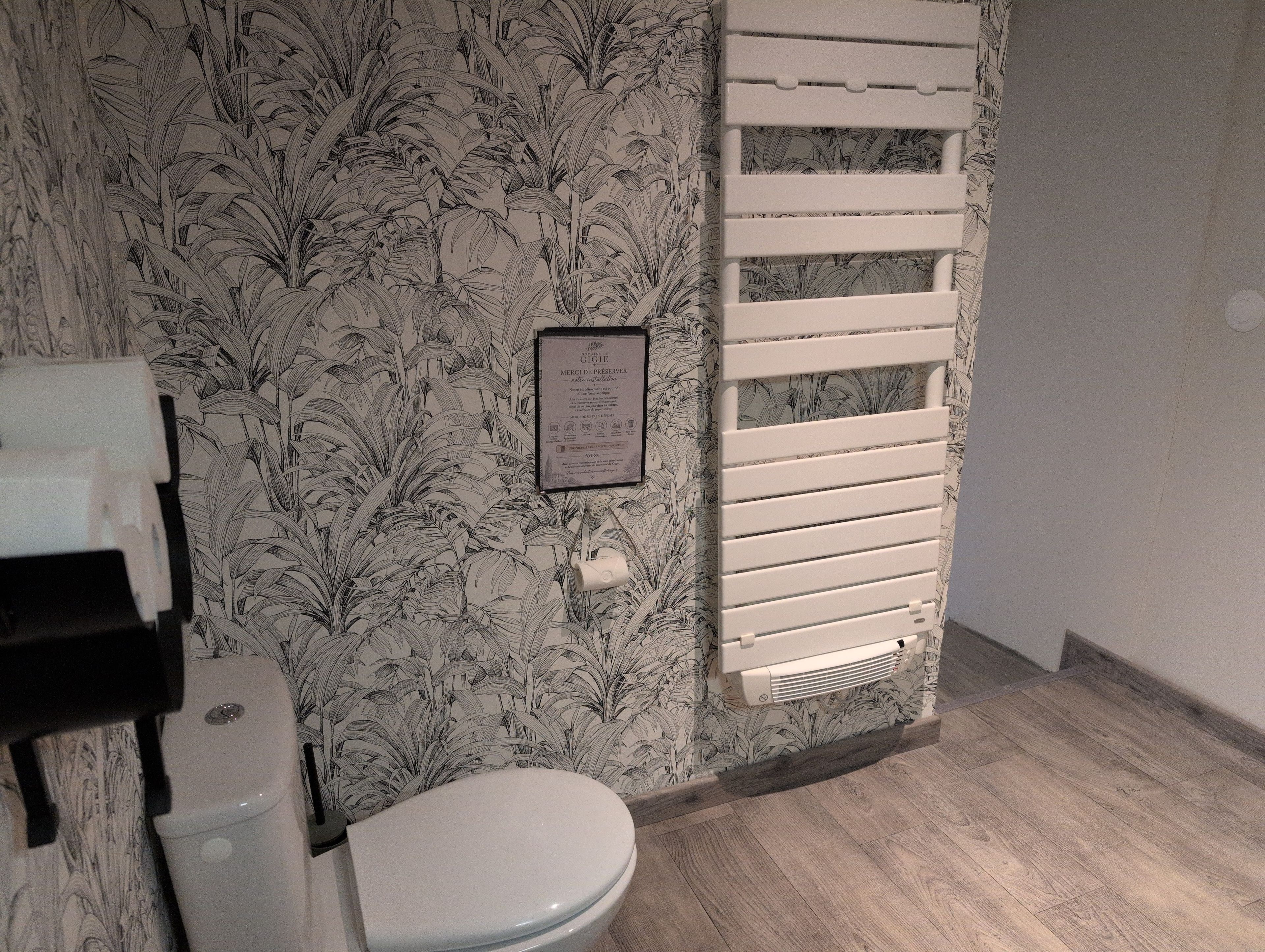 A bathroom with a toilet, a radiator, and a wall with a floral pattern.