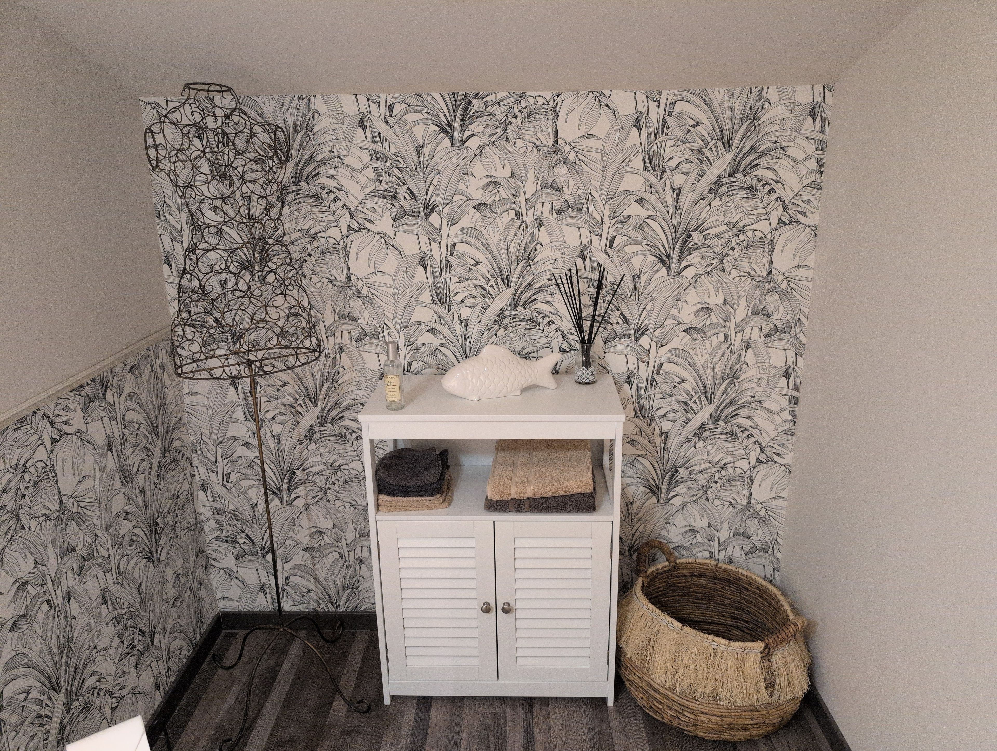 A room with a white cabinet, a woven basket, and a wall with a leaf pattern.
