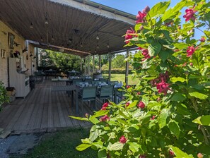 An outdoor dining area with tables and chairs, a covered seating area, and a garden with flowering plants. - Bed and Breakfast 'Suite Familiale' with Shared Pool, Shared Terrace and Wi-Fi (La Devise)