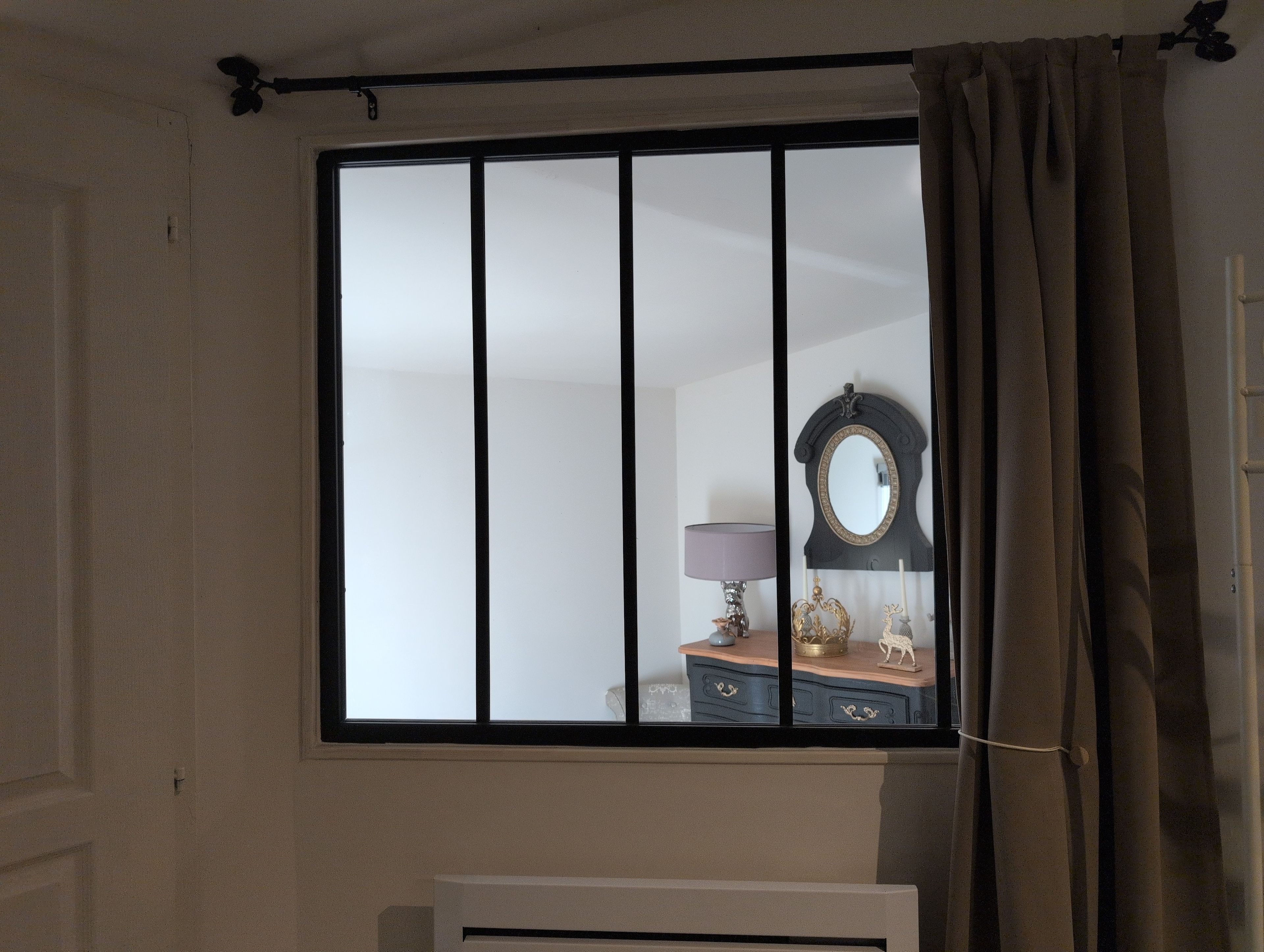 Una habitación con ventana, espejo y cómoda con adornos.