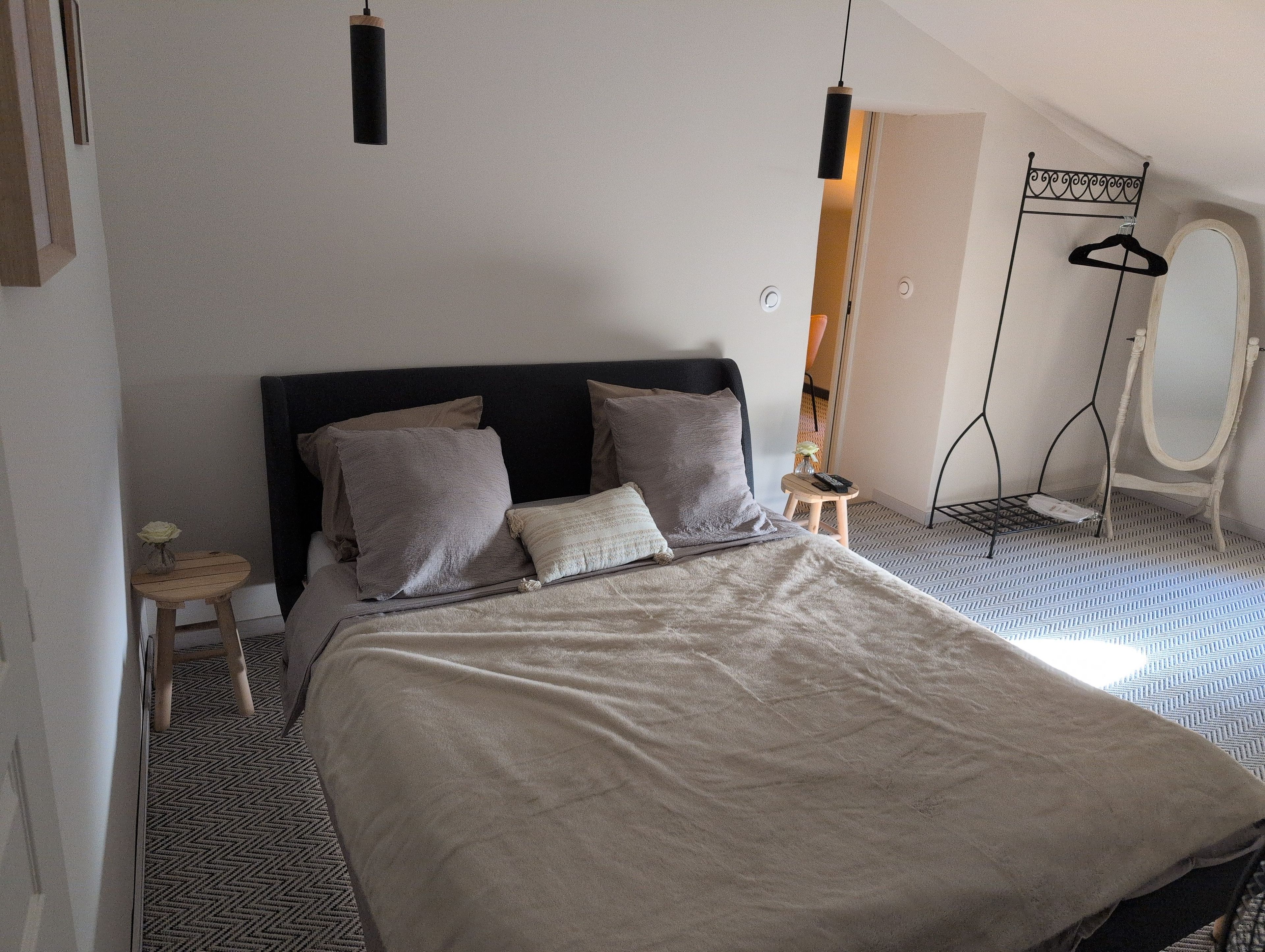 A bedroom with a bed, bedside tables, a hanging light, and a mirror.