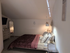 A bedroom with a bed, dresser, mirror, bedside table, lamp, and a wall-mounted decoration. - Bed and Breakfast 'Suite Familiale' with Shared Pool, Shared Terrace and Wi-Fi (La Devise)
