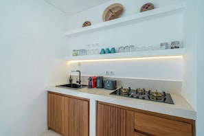 A modern kitchen with a countertop, sink, stove, and shelves above. - Villa Dara & Villa Irena (Canggu)