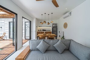 A modern living room with a grey sofa, wooden ceiling fan, and pendant lights. - Villa Dara & Villa Irena (Canggu)