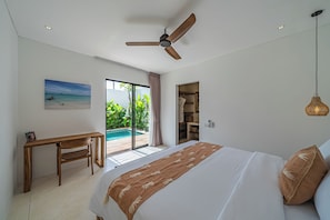 A bedroom with a bed, a desk, a ceiling fan, and a view of a pool and greenery. - Villa Dara & Villa Irena (Canggu)