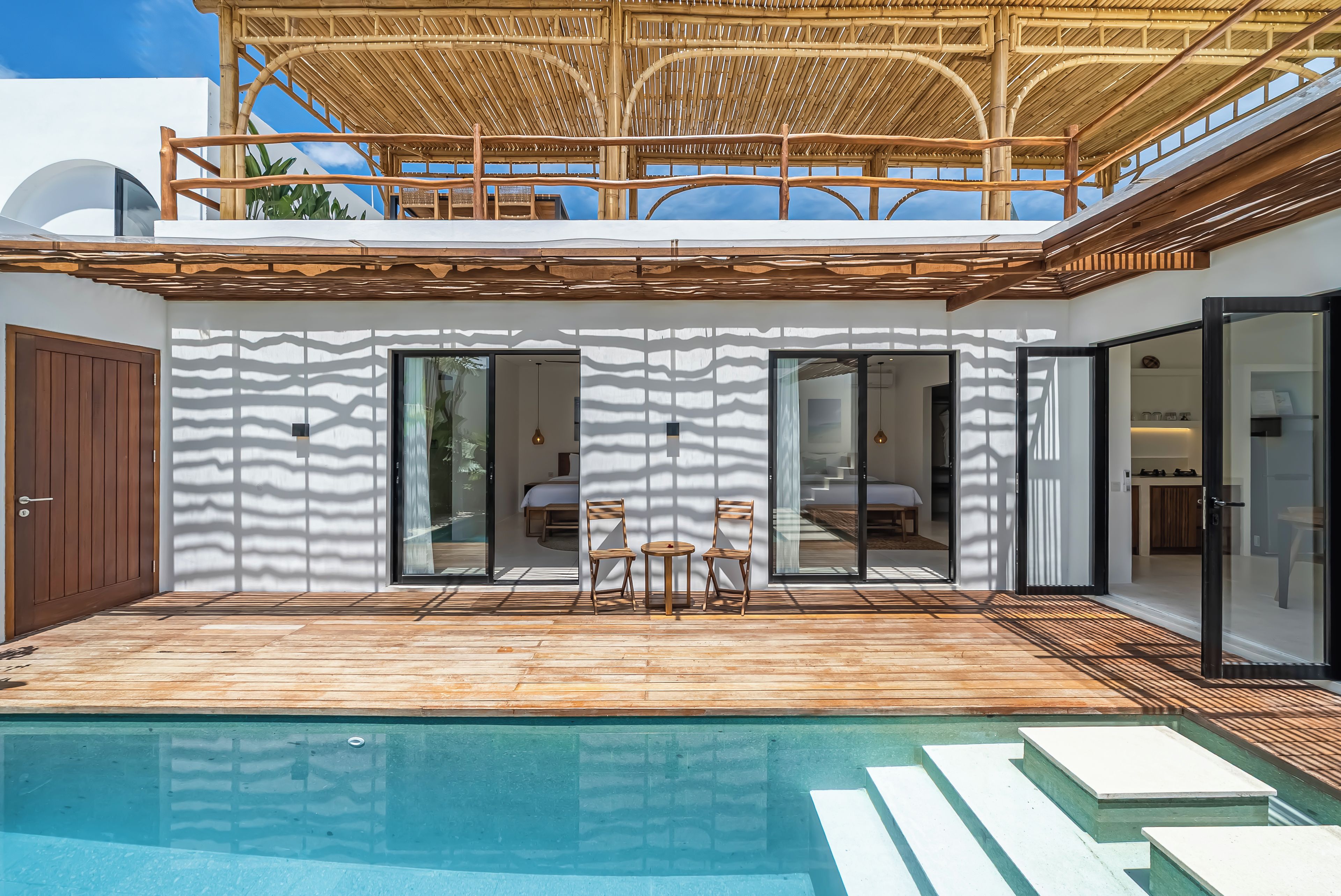 Una casa moderna con piscina, terraza de madera y un espacio exterior cubierto con sillas.
