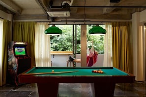 A pool table with balls, a pool cue, and a video game machine in a room with windows and curtains. - Max Brown Hotel Downtown, part of Sircle Collection - Suite (Athens)