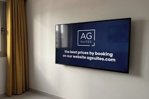 A flat-screen TV mounted on a wall displaying a logo and text for AG Suites, advertising the best prices by booking on their website. - Rocha Golden Cliff by Agsuites com (Portimão)