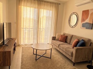 A living room with a sofa, a coffee table, a TV stand, and a large window with curtains. - Rocha Golden Cliff by Agsuites com (Portimão)