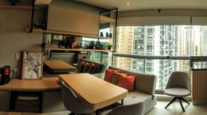 A modern living room with a dining area, a sofa with cushions, a small table, and a view of high-rise buildings through large windows. - Studio - Berrini/ Faria Lima/ CGH Airport (São Paulo)