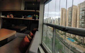 Interior moderno com varanda e vista para a cidade, incluindo um espaço de estar com almofadas e uma mesa de jantar.