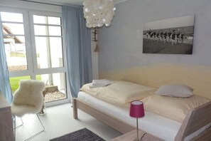 A bedroom with a bed, a chair, a lamp, and a window with curtains. - "Castle by the Sea" - Apt. 02 (Wyk auf Föhr)