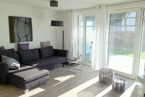 A modern living room with a sofa, coffee table, and a large window with a view. - "Castle by the Sea" - Apt. 02 (Wyk auf Föhr)