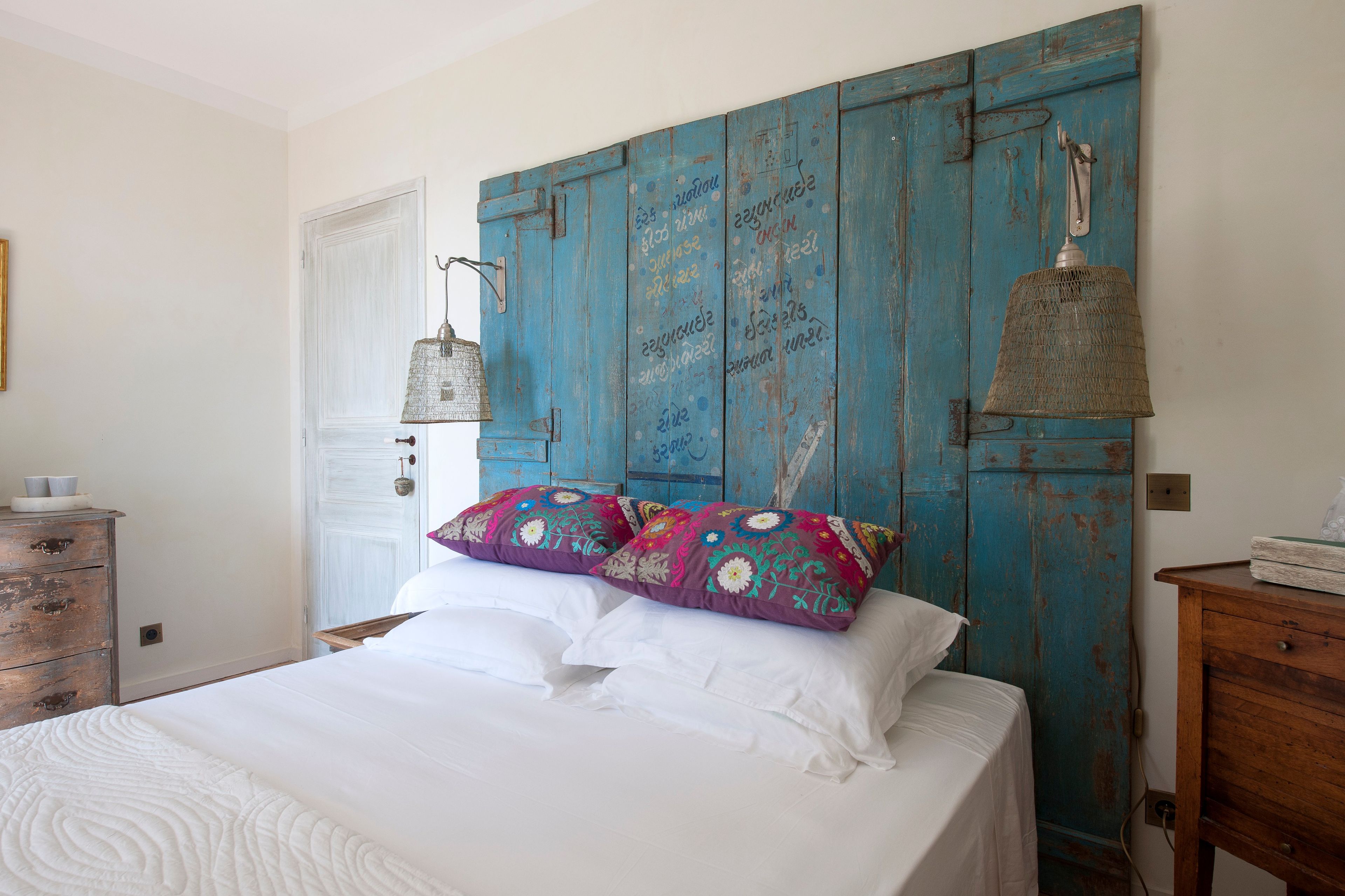A bedroom with a bed, a dresser, and a blue-painted headboard with decorative elements.