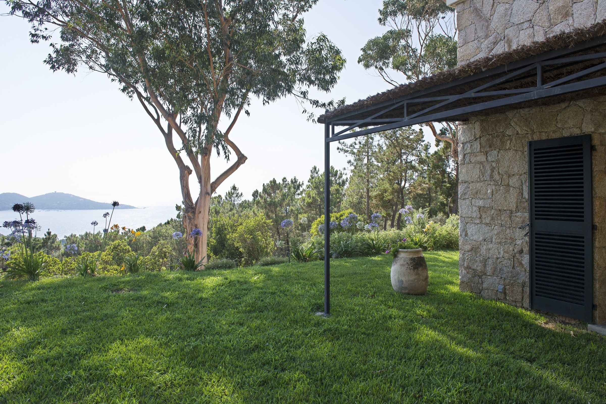 Un jardin avec un grand arbre, un bâtiment en pierre et une vue sur la mer.