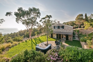 A stone house with a patio, surrounded by lush greenery and a view of the sea. - Villa 'La Bergerie' with Sea View, Wi-Fi and Air Conditioning (Coti-Chiavari)