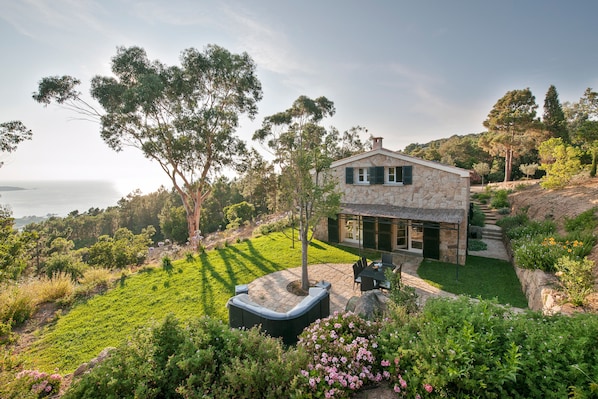 A stone house with a patio, surrounded by lush greenery and a view of the sea. - Villa 'La Bergerie' with Sea View, Wi-Fi and Air Conditioning (Coti-Chiavari)