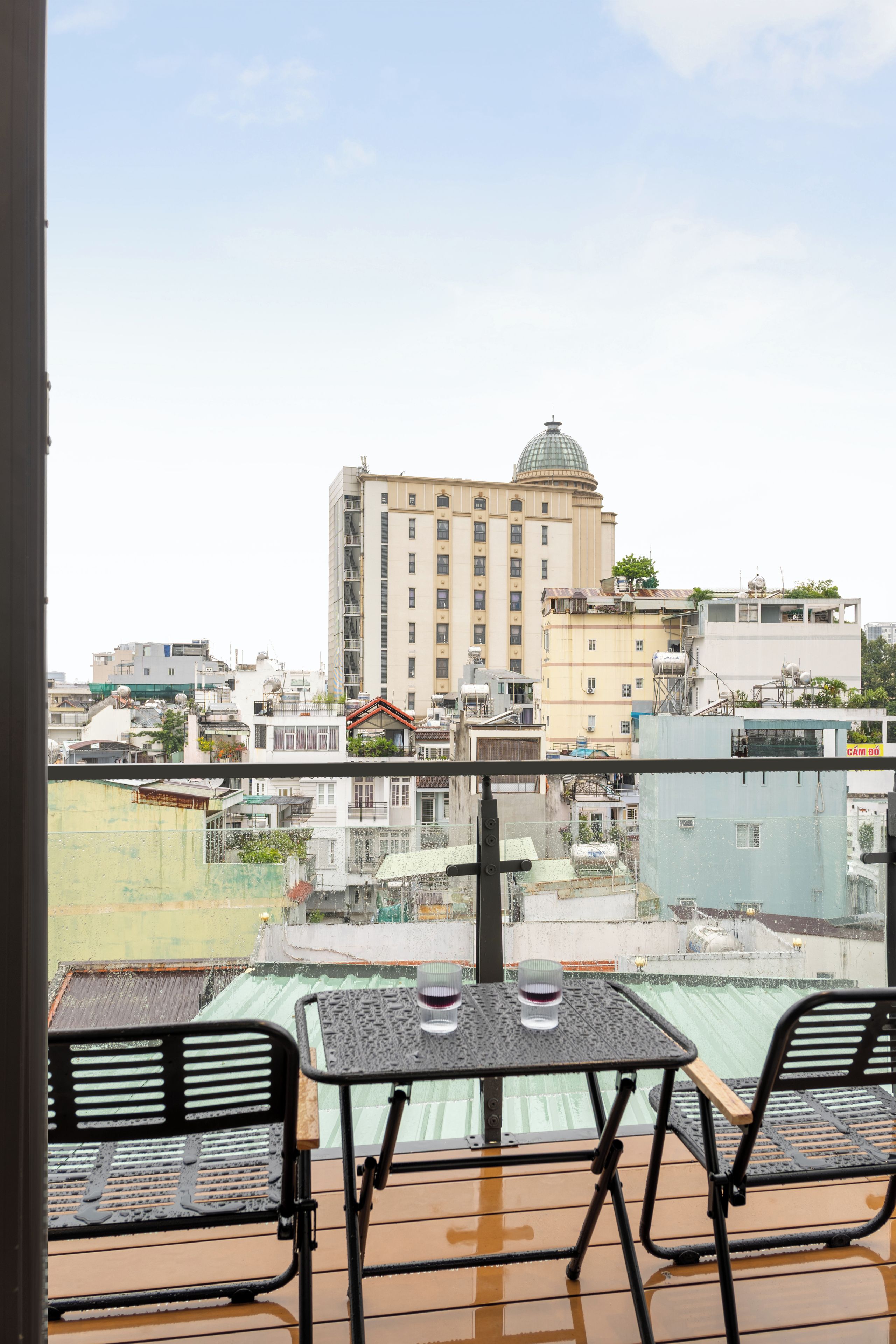 Uma varanda com mesa e cadeiras, com vista para um horizonte urbano com diversos edifícios, incluindo um prédio imponente com cúpula.