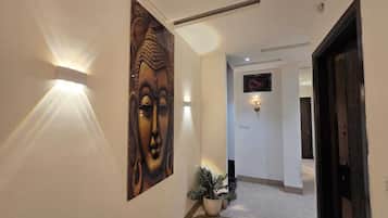 Un pasillo con un cuadro de Buda, apliques de pared, una planta en maceta y una puerta.
