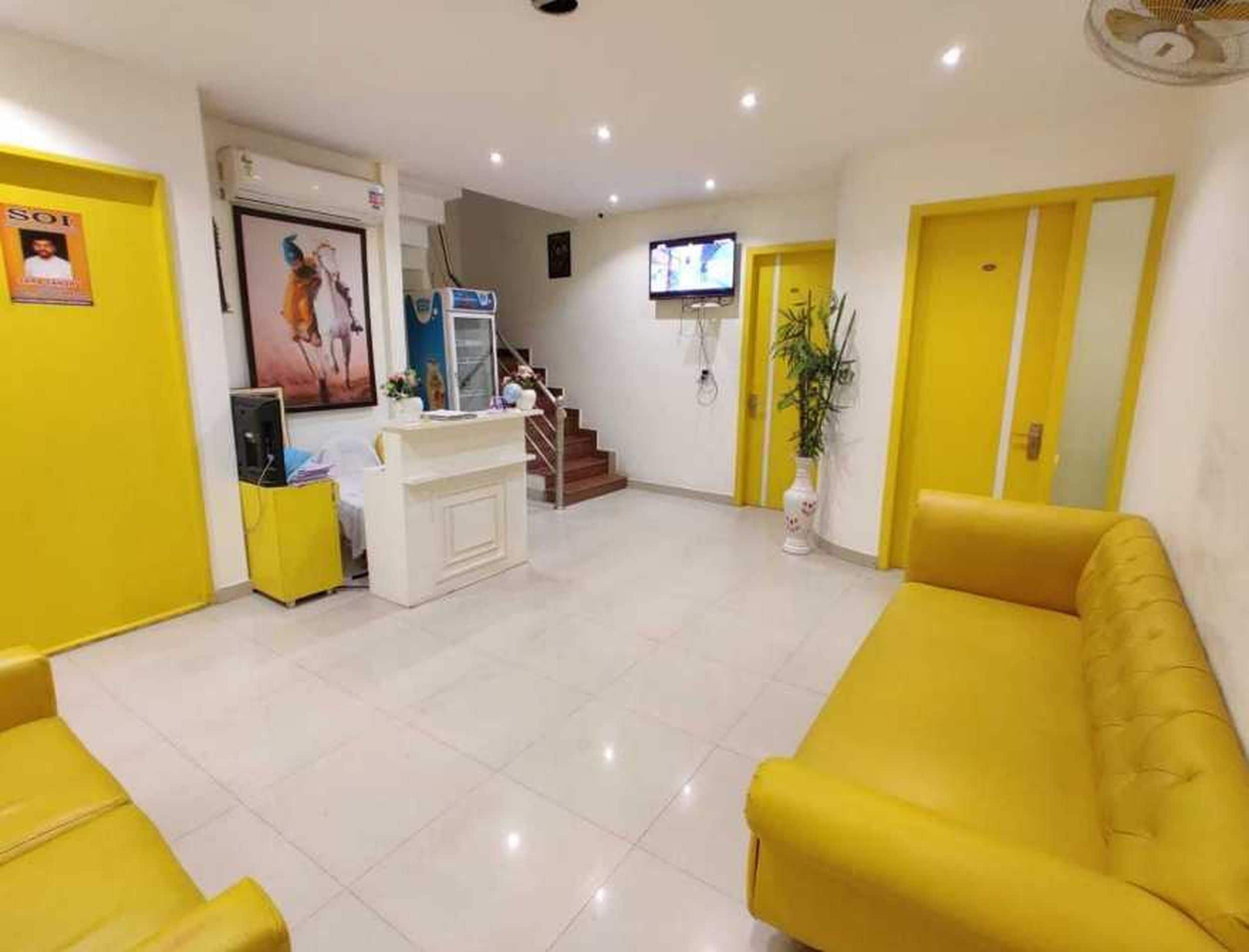 A reception area with a reception desk, a television mounted on the wall, a staircase leading to an upper floor, and yellow walls and furniture.
