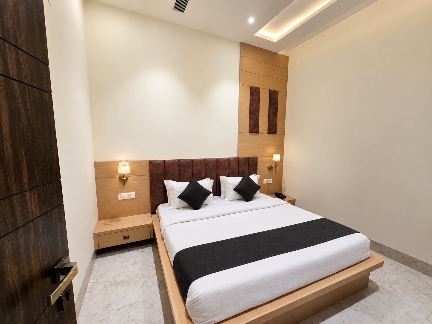 Habitación de hotel moderna con una cama grande, cabecero de madera, lámparas de noche y suelo de mármol.