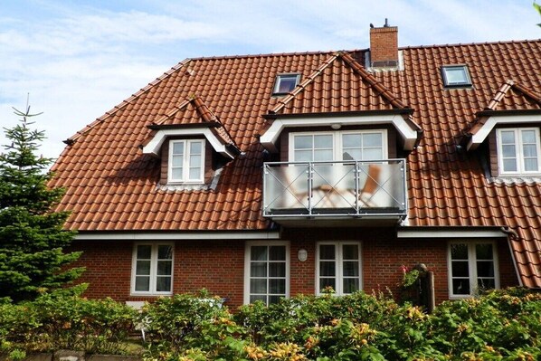 Et toetagers hus med rødt tegltag, ovenlys og en balkon.