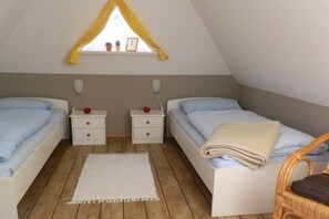 Une chambre avec deux lits, une fenêtre avec des rideaux jaunes, un tapis blanc et un plancher en bois.