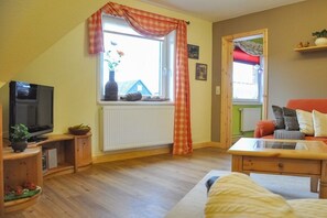 Ein Wohnzimmer mit Fernseher, einem fenster mit Vorhängen, einem Sofa und einem Couchtisch aus Holz.