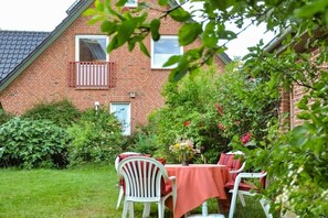Ein Backsteinhaus mit rotem Dach, einem Balkon und einem Garten mit Tisch und Stühlen.