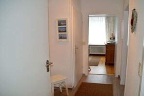 A hallway with a door leading to a room with a radiator and a window with curtains. - Flurstraße - OG right (Wyk auf Föhr)