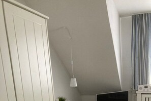 A room with a white wardrobe, a hanging light fixture, a television, and a radio on a table. - Flurstraße - OG links (Wyk auf Föhr)