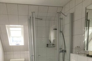 En dusch med en glasdörr, ett fönster och en spegel.