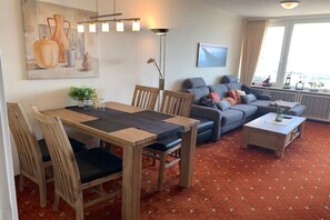 Ein möbliertes Wohnzimmer mit Essbereich, einer Sofagarnitur, einem Couchtisch und einem Gemälde an der Wand.