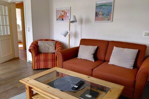 Ein Wohnzimmer mit Sofa, Sessel und Couchtisch mit Fernbedienung.