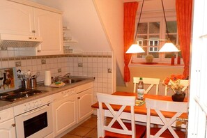 Cocina con gabinetes blancos, estufa y lavamanos. Hay una mesa de comedor con sillas y una ventana con cortinas.
