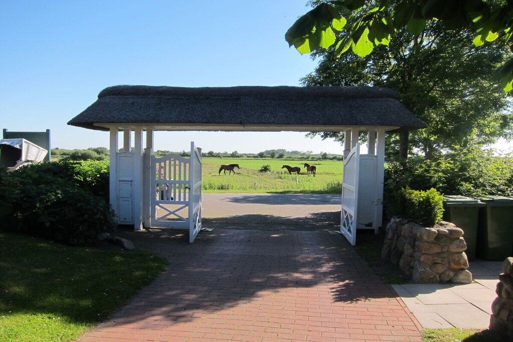A gated entrance with a thatched roof structure, a paved pathway, and horses in the background.