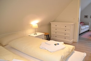 A bedroom with a bed, a nightstand, a dresser, and a small stool. - Holiday home with 1 bedroom (Wyk auf Föhr)