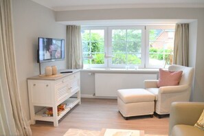 A modern living room with a television, a white cabinet, and a comfortable seating area. - Holiday home with 1 bedroom (Wyk auf Föhr)